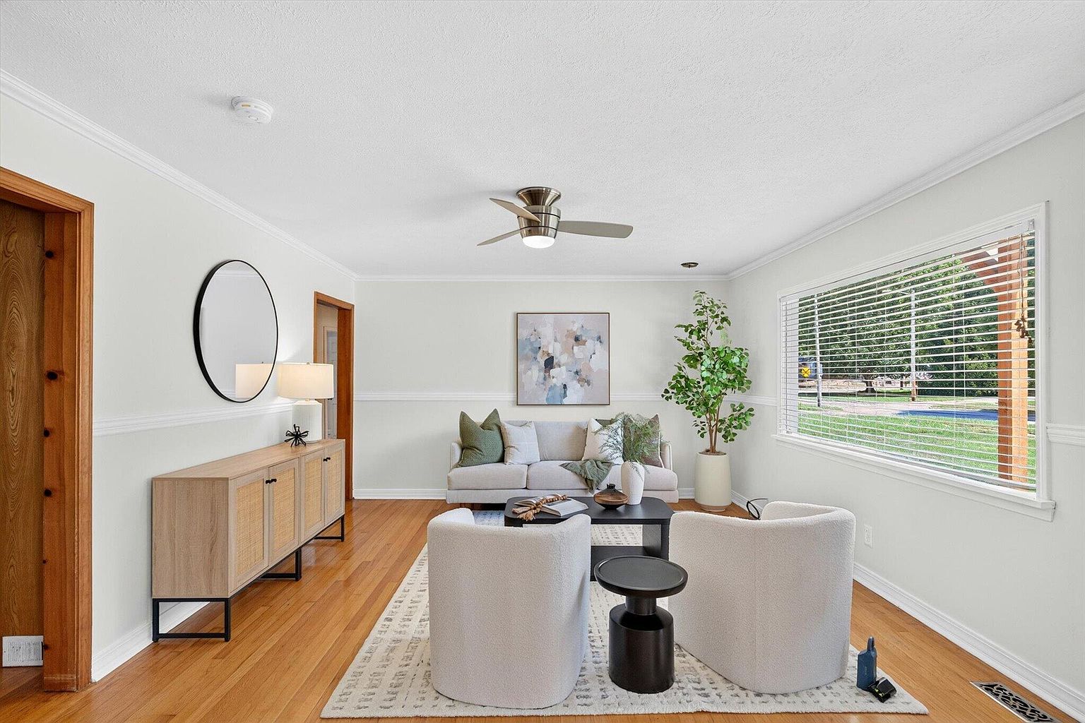 Living room with picture window, boucle chairs and round mirror over the sideboard - 1345 E Walnut St, Springfield, MO home staging