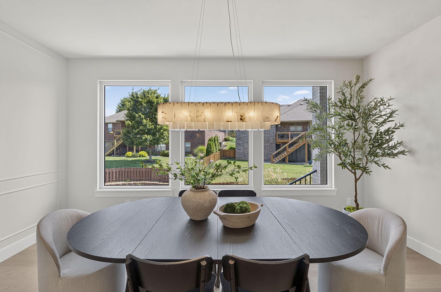 Dining area with black oval table, cream upholstered chairs and linear chandelier under backyard windows - 2050 N Silver Charm Ave, Springfield, MO