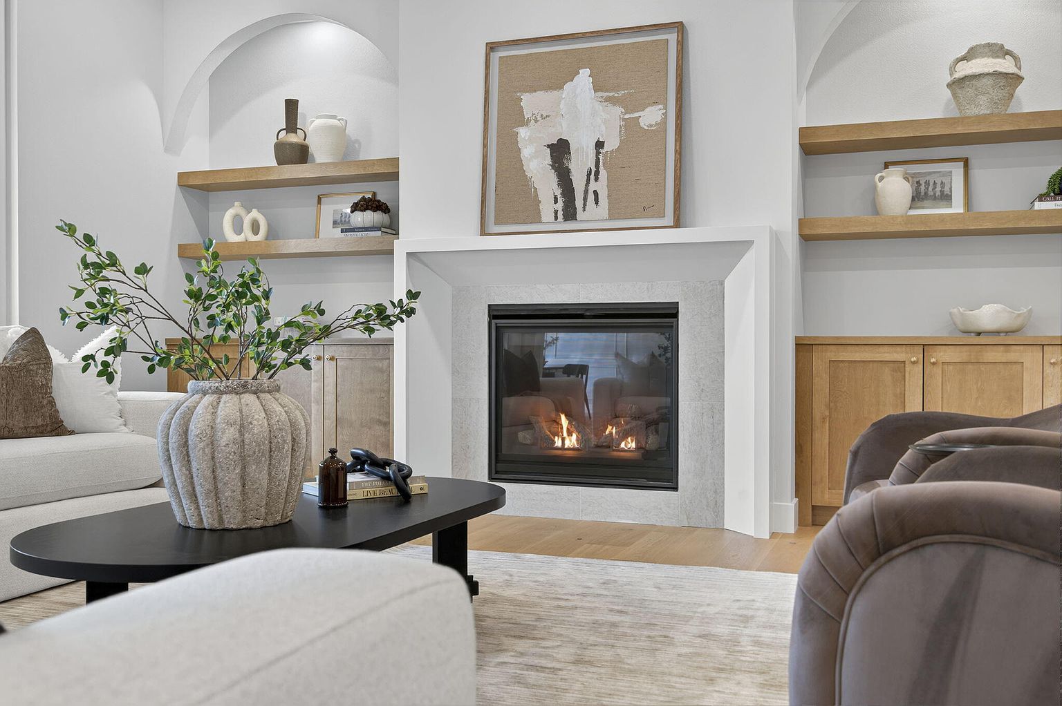 Fireplace with abstract art and arched niches over wood built-ins, styled coffee table in the foreground - 2050 N Silver Charm Ave, Springfield, MO