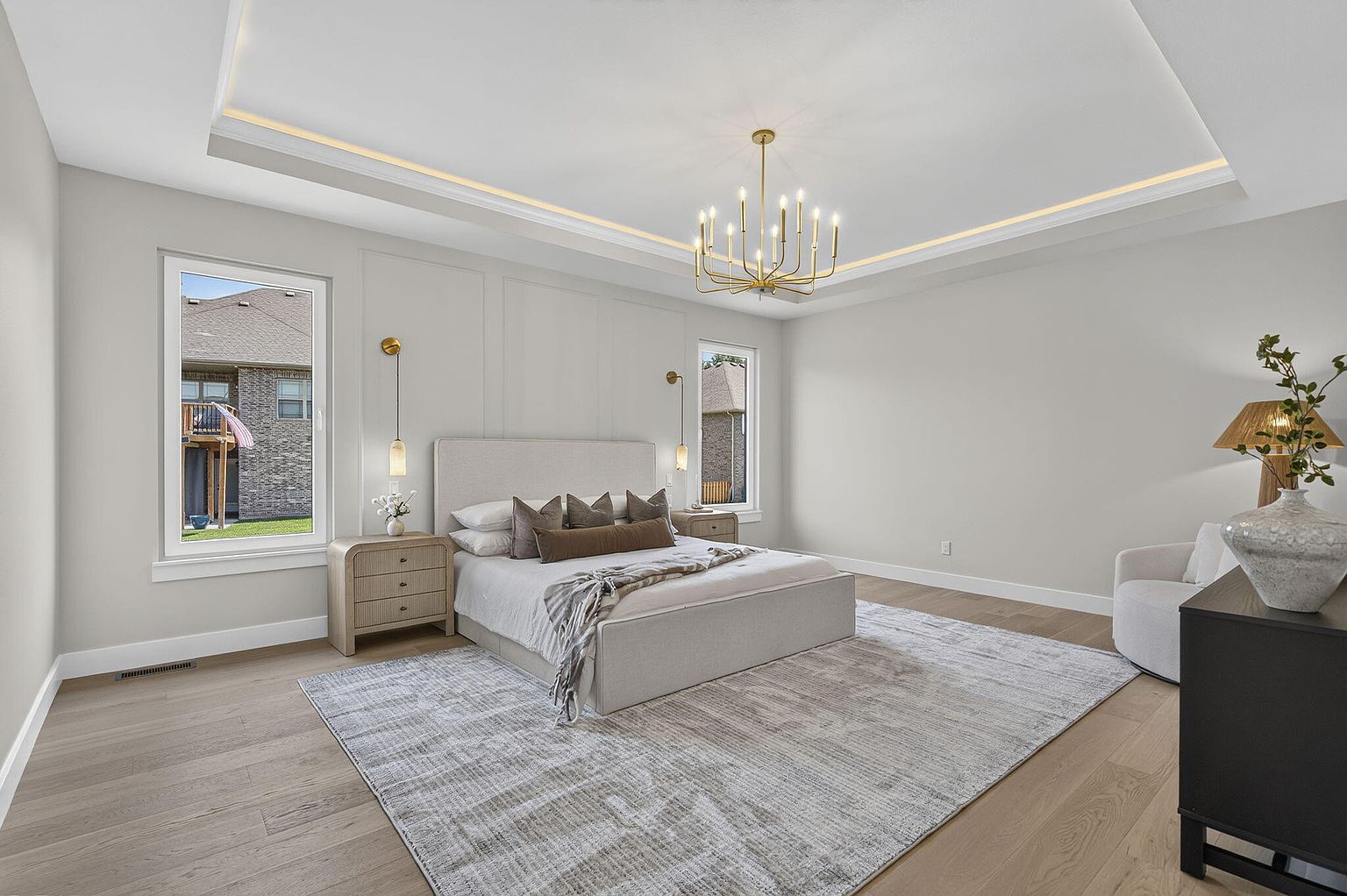Primary bedroom with lighted tray ceiling, gold chandelier, upholstered bed and patterned rug after staging at 2050 N Silver Charm Ave, Springfield, MO