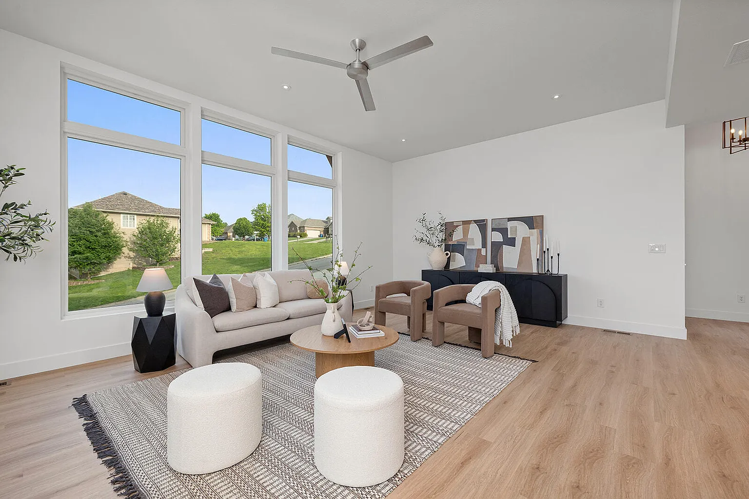 Staged living room with white ottomans and floor-to-ceiling windows - 2807 S 14th Ave, Ozark, MO