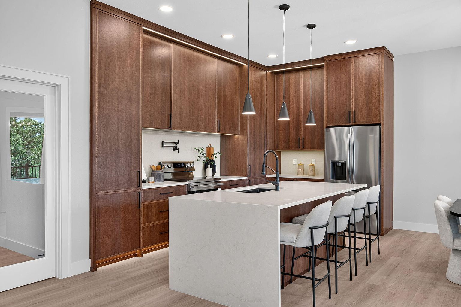 Kitchen with dark wood cabinetry, waterfall quartz island, black pendants and white bar stools - 346 Sunset Dr, Saddlebrooke, MO