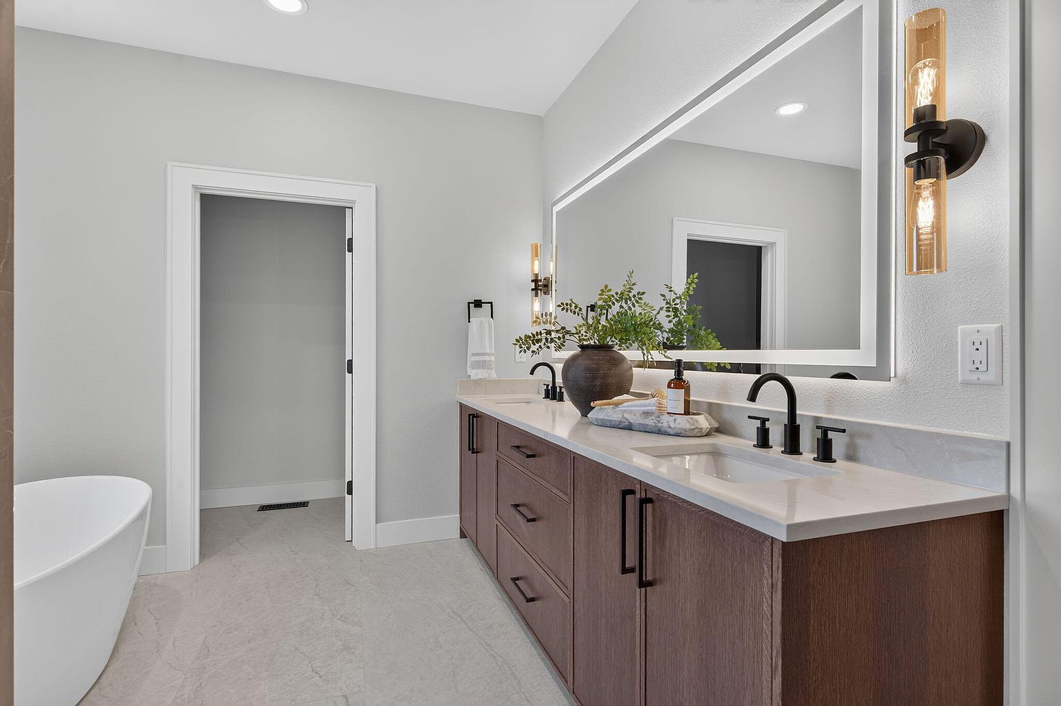 Primary bathroom with wood double vanity, lighted mirror and freestanding tub after staging at 346 Sunset Dr, Saddlebrooke, MO