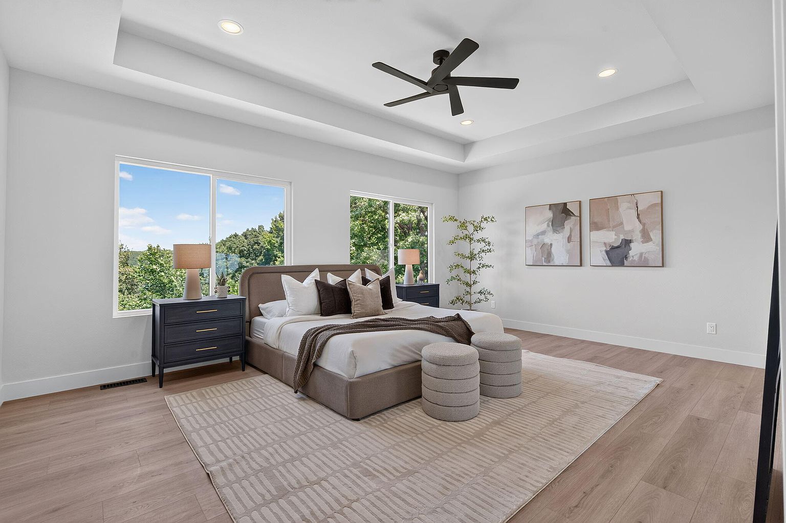 Primary bedroom with tray ceiling, upholstered bed, black nightstands and wooded views after staging at 346 Sunset Dr, Saddlebrooke, MO