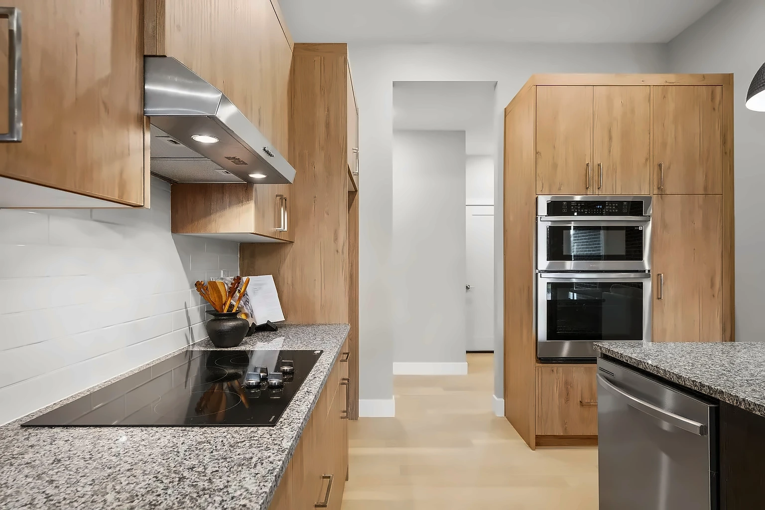 Kitchen with stainless range hood, cooktop and double wall ovens looking down the hallway - 5048 Swale home staging, Springfield, MO