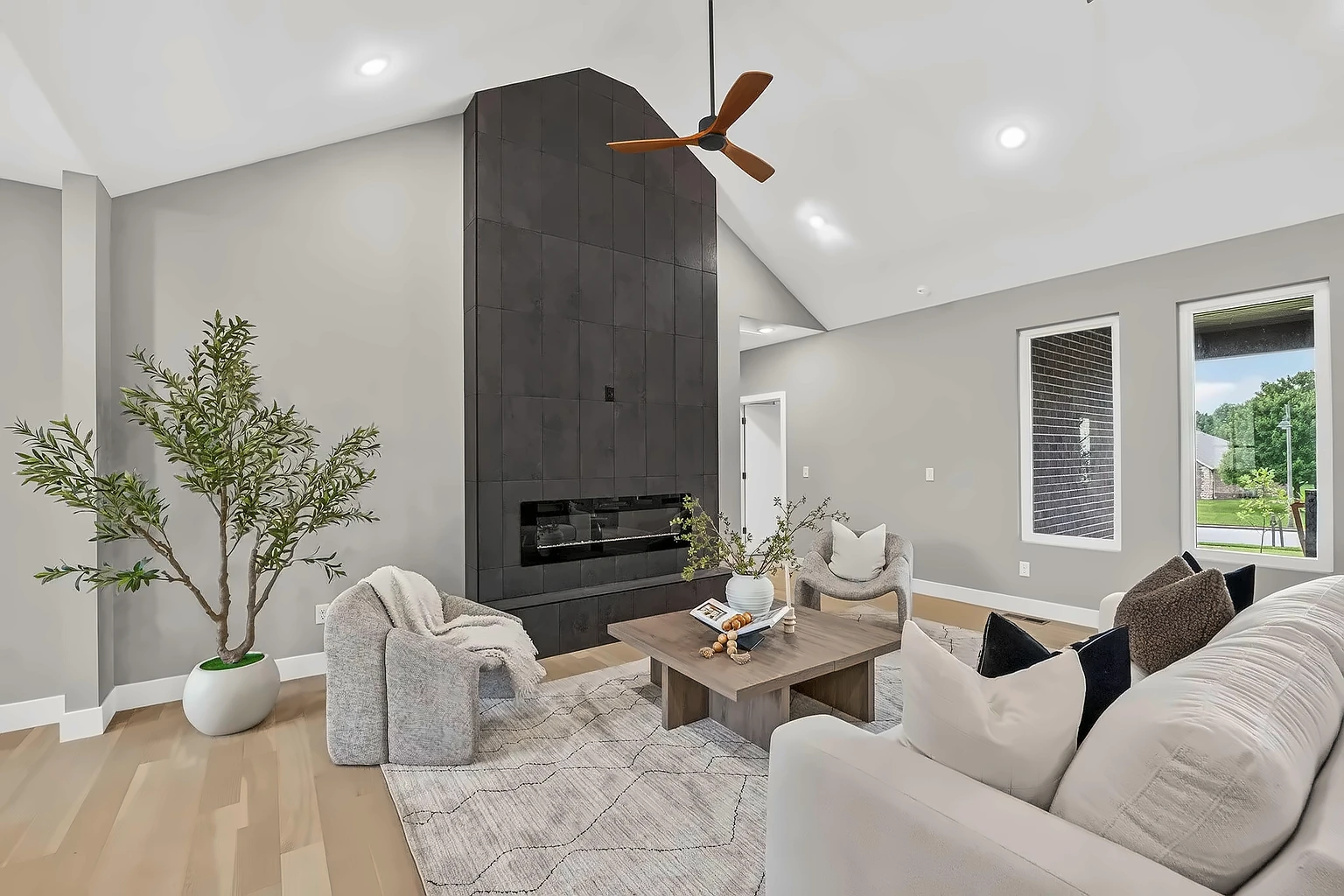Living room with floor-to-ceiling dark tile fireplace, white sofa, boucle swivel chair and olive tree - 5048 Swale home staging, Springfield, MO