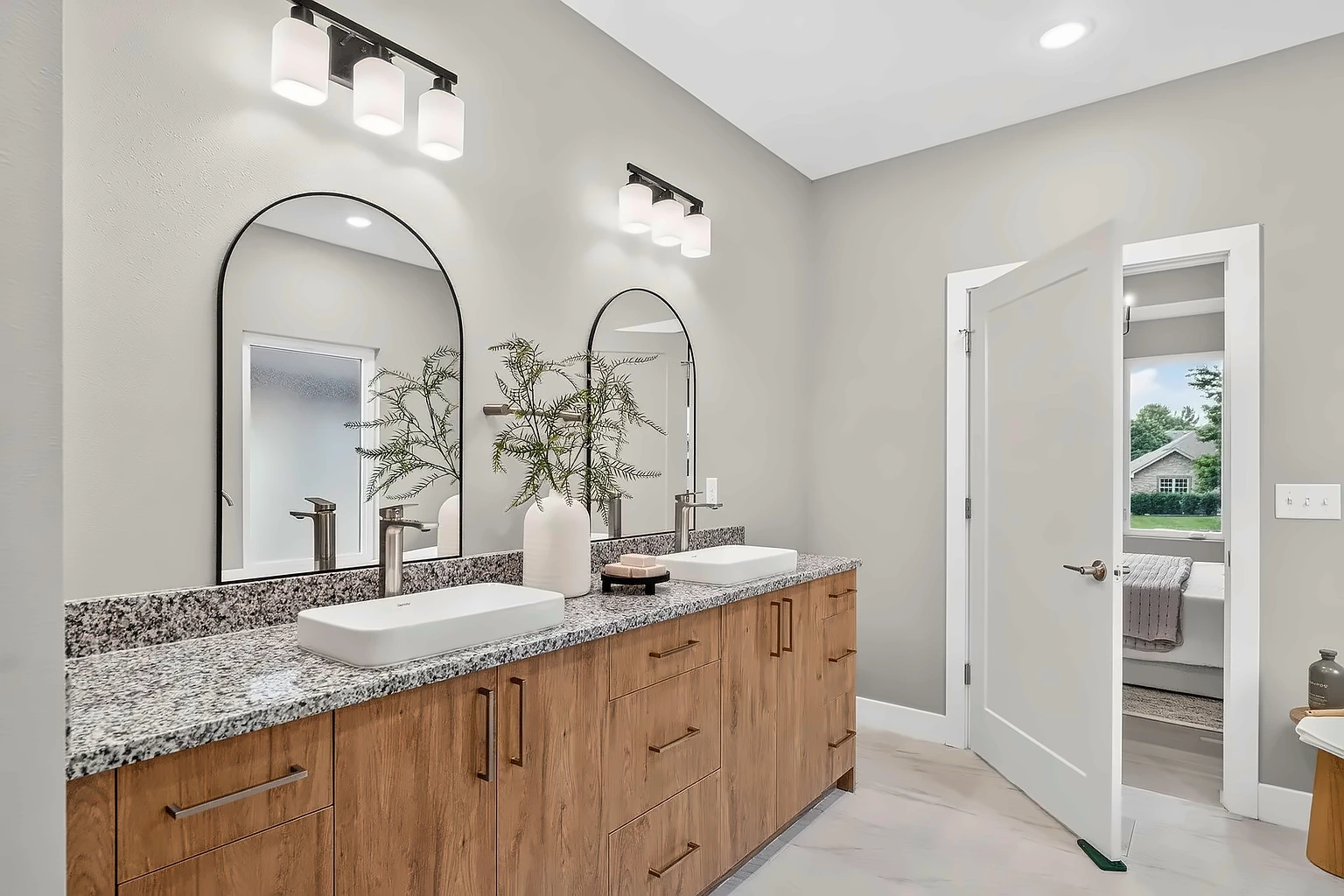 Primary bathroom with double granite vanity, warm wood cabinets and arched mirrors after home staging at 5048 Swale, Springfield, MO