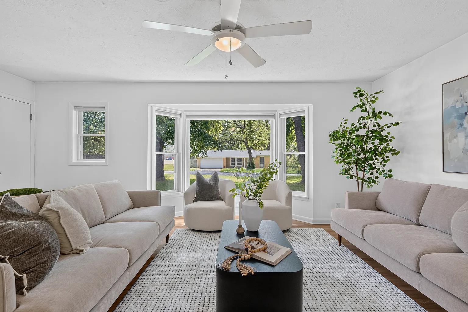 Living room bay window with facing sofas, swivel chairs and black coffee table - Florence Ave home staging, Springfield, MO