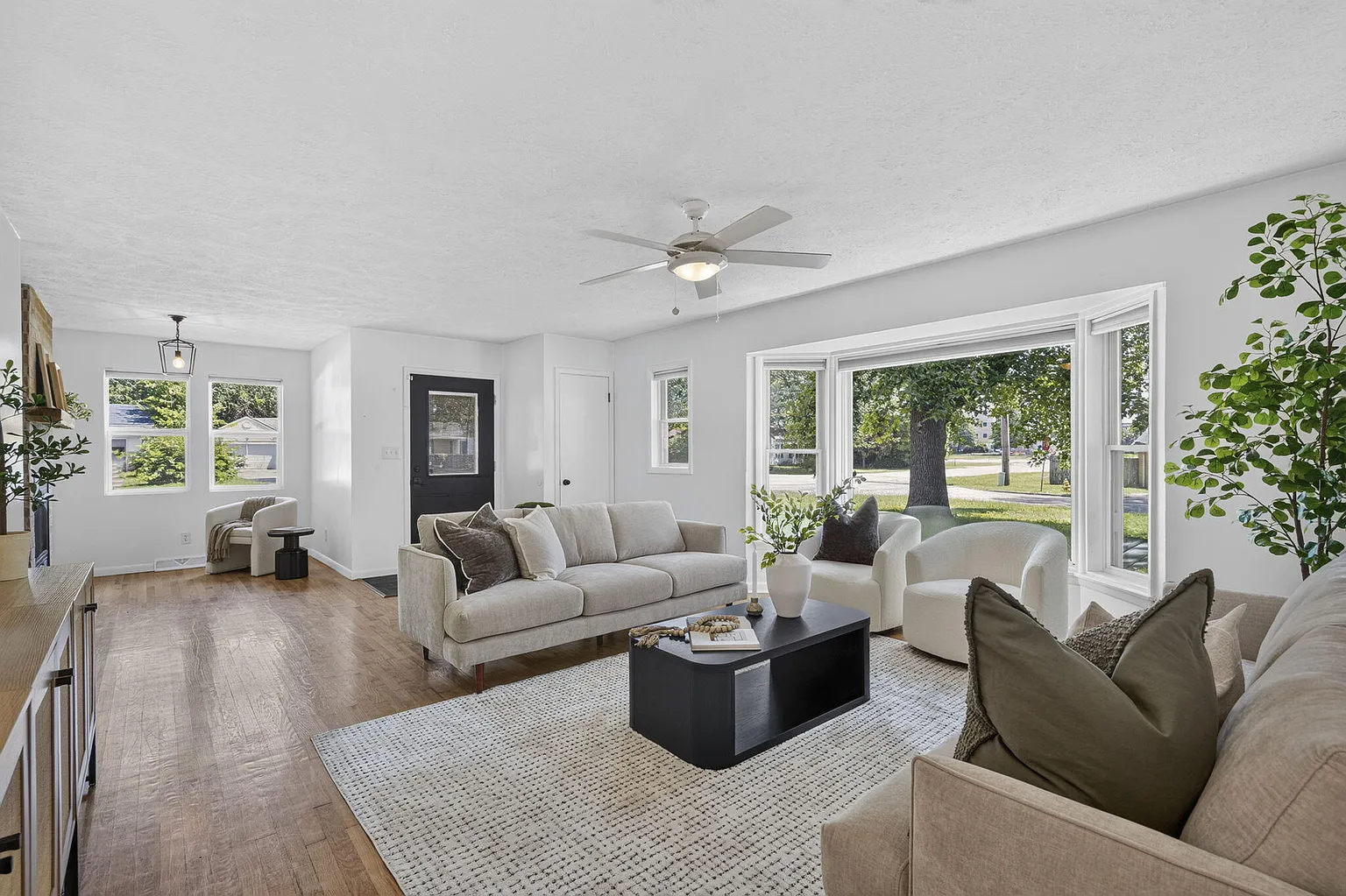 Living room wide angle with bay window, neutral sofas and black entry door after vacant home staging on Florence Ave, Springfield, MO
