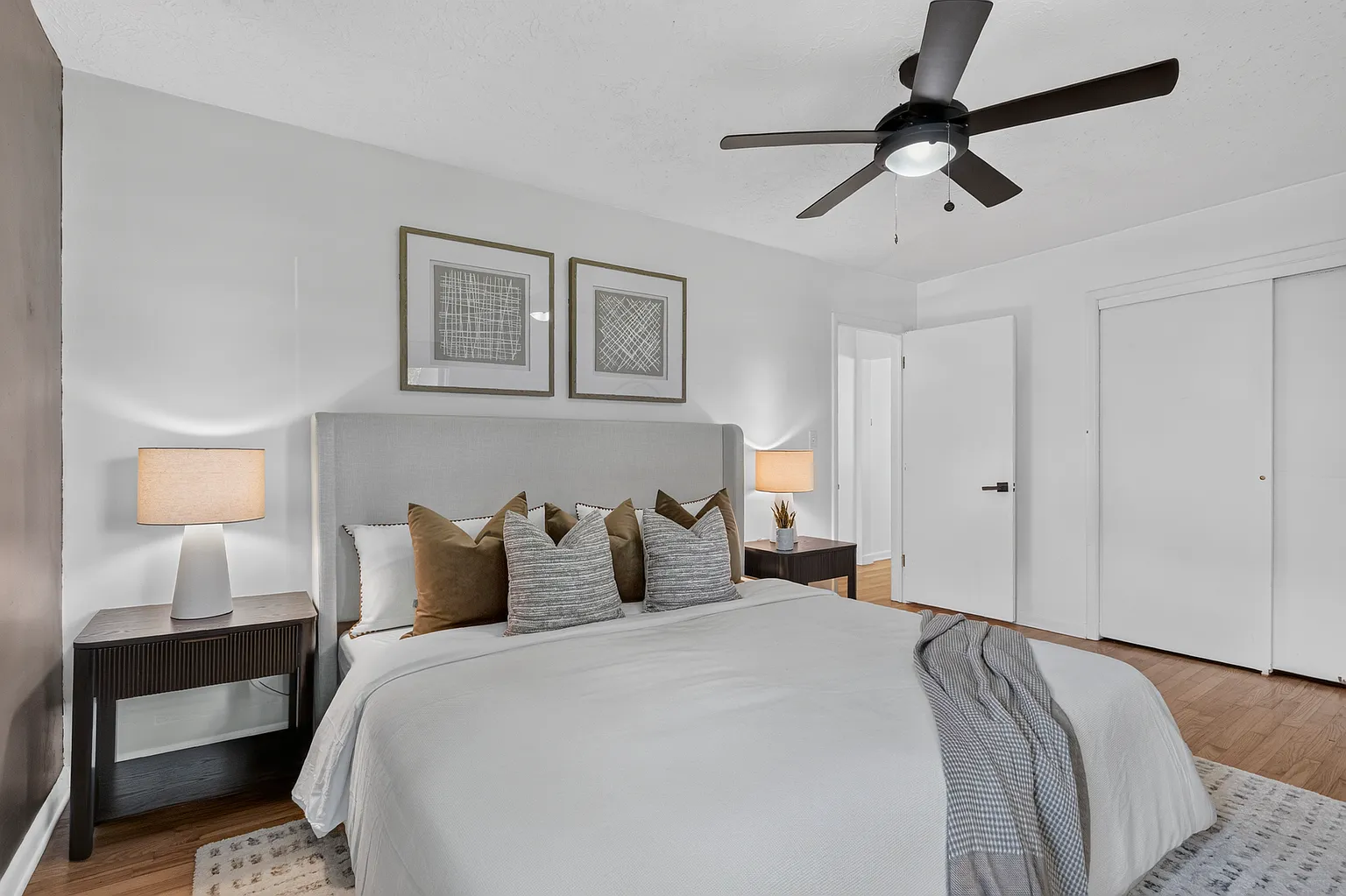 Primary bedroom with upholstered headboard, layered pillows and dark nightstands after staging - Florence Ave, Springfield, MO