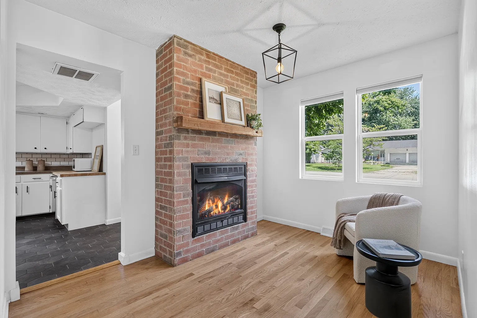 Sitting area with exposed brick fireplace, wood mantel and boucle accent chair after home staging - Florence Ave, Springfield, MO