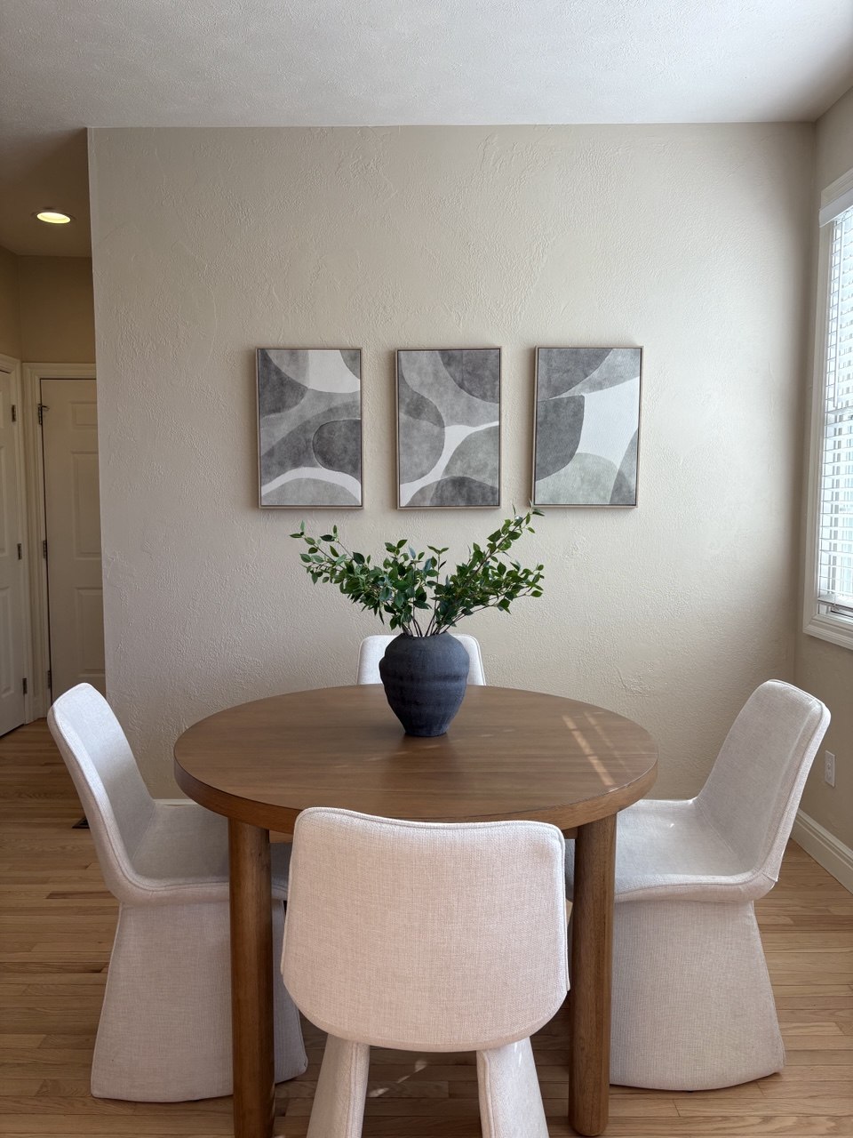 Breakfast nook with round wood table, white chairs and abstract triptych wall art - Gaslight Drive, Springfield, MO home staging