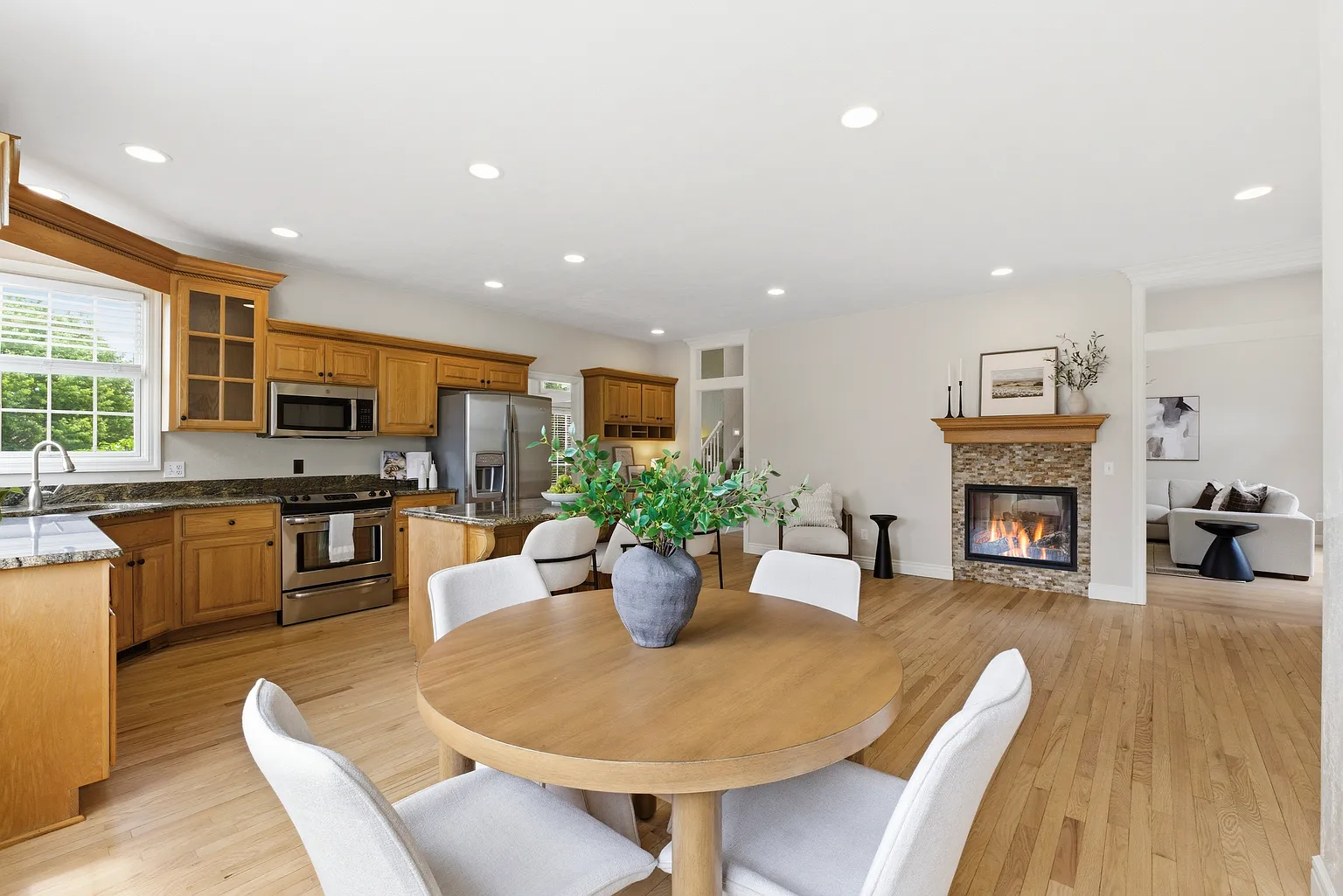 Open-concept kitchen and dining with oak cabinets, granite counters and fireplace view after staging - Gaslight Drive, Springfield, MO
