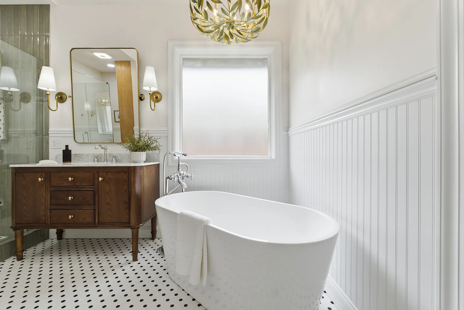 Primary bathroom freestanding tub with brown vanity, brass sconces and olive branch chandelier - Gaslight Drive, Springfield, MO home staging