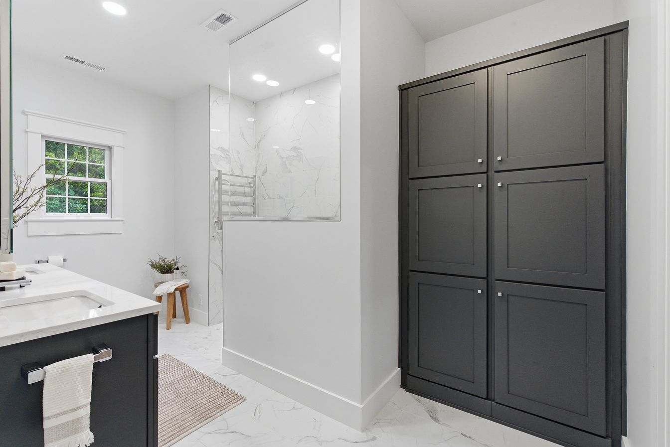 Primary bathroom with charcoal linen cabinets, marble floors and staged vanity decor - Wilderness Road, Rogersville, MO