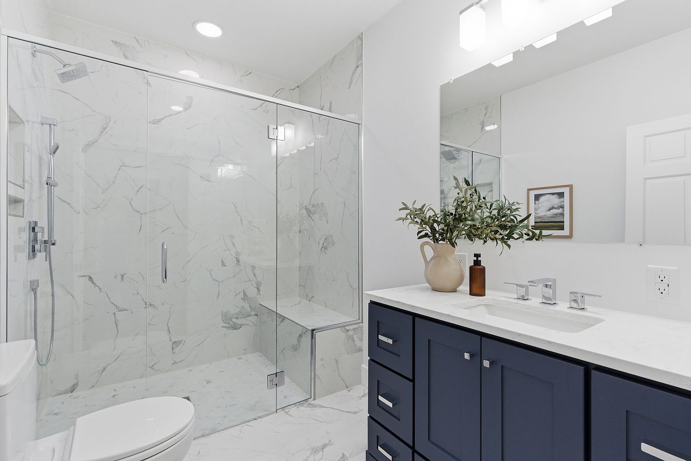 Bathroom with navy vanity, marble walk-in shower and olive branch styling after staging - Wilderness Road, Rogersville, MO