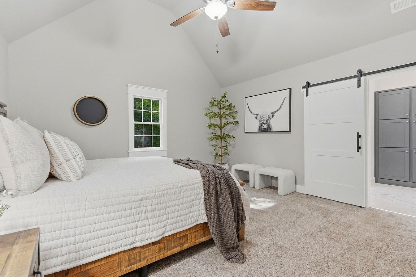 Bedroom with white barn door, highland cow art and wood bed after vacant home staging - Wilderness Road, Rogersville, MO